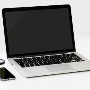 A minimalist workspace featuring a laptop, smartphone, and an apple on a clean white desk.