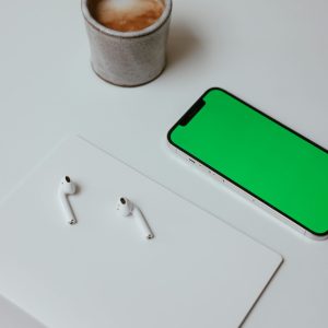 Stylish workspace setup with coffee, earpods on a tablet, and smartphone with green screen.